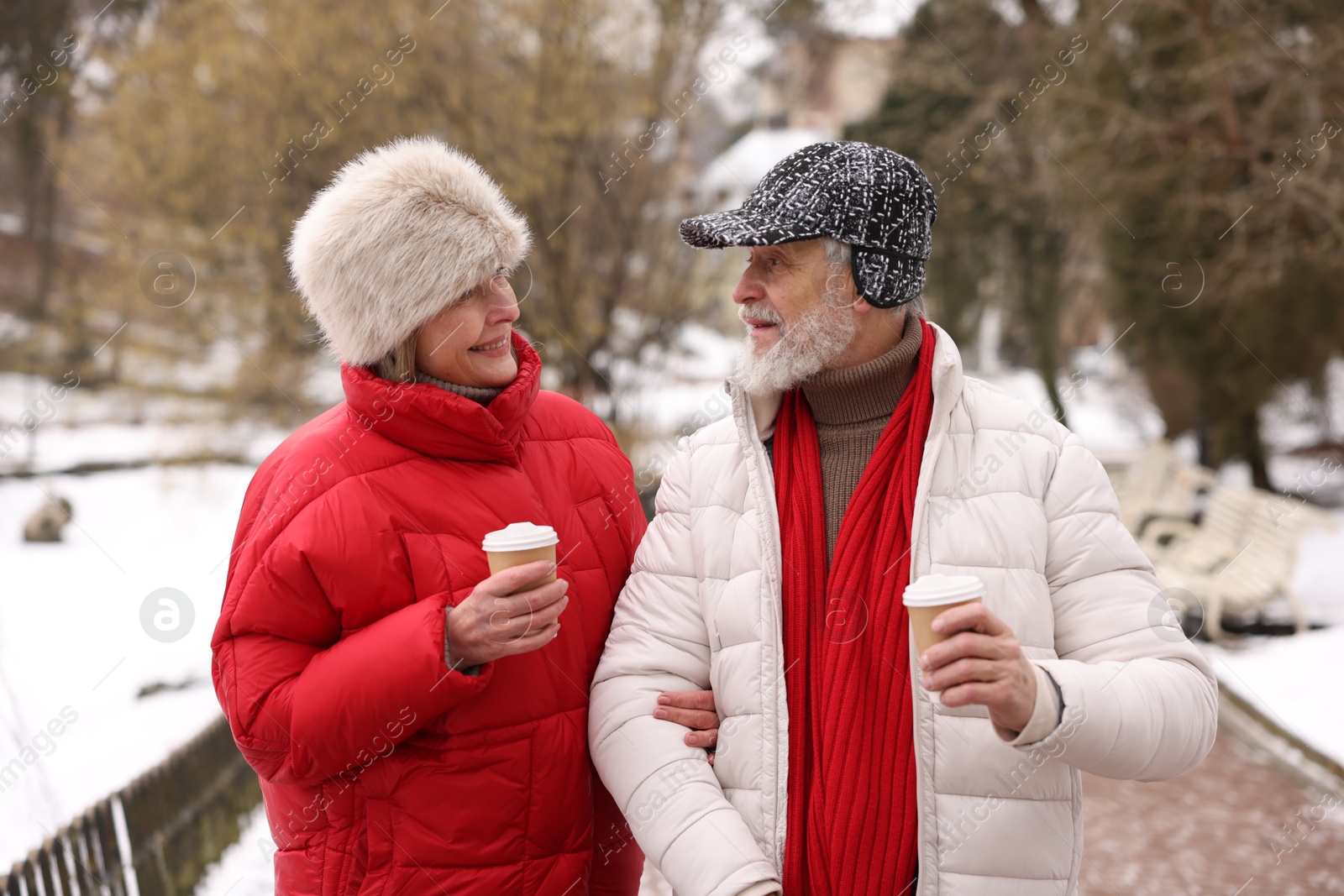 Photo of Happy senior couple with paper cups walking at winter park