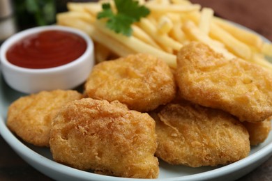 Photo of Tasty chicken nuggets and french fries with sauce on wooden table, closeup