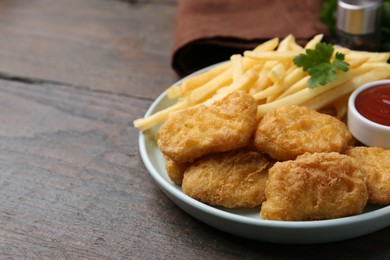 Photo of Tasty chicken nuggets and french fries with sauce on wooden table, closeup. Space for text