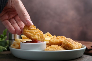 Photo of Woman eating tasty chicken nuggets and french fries with sauce at wooden table, closeup. Space for text