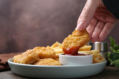 Photo of Woman eating tasty chicken nuggets and french fries with sauce at wooden table, closeup. Space for text