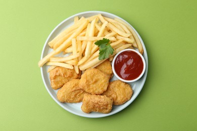 Photo of Tasty chicken nuggets and french fries with sauce on green background, top view