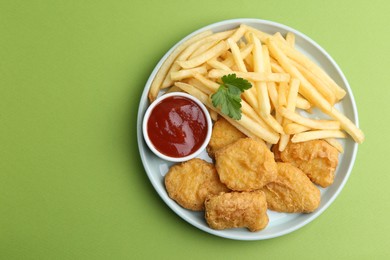 Photo of Tasty chicken nuggets and french fries with sauce on green background, top view. Space for text