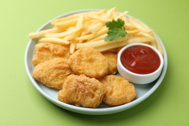 Photo of Tasty chicken nuggets and french fries with sauce on green background, closeup