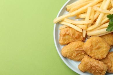 Photo of Tasty chicken nuggets and french fries on green background. Space for text