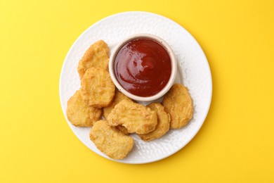 Photo of Tasty chicken nuggets with sauce on yellow background, top view