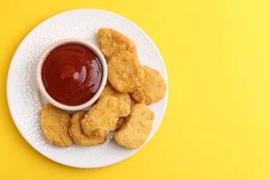 Photo of Tasty chicken nuggets with sauce on yellow background, top view. Space for text