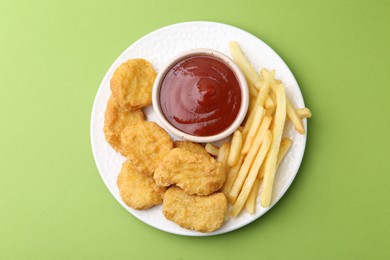 Photo of Tasty chicken nuggets and french fries with sauce on green background, top view
