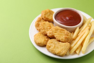Photo of Tasty chicken nuggets and french fries with sauce on green background, closeup. Space for text