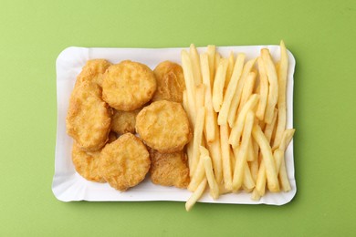 Photo of Tasty chicken nuggets and french fries on green background, top view