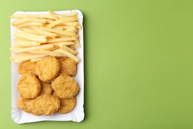 Photo of Tasty chicken nuggets and french fries on green background, top view. Space for text