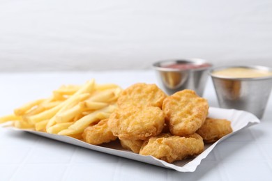 Photo of Tasty chicken nuggets and french fries with sauce on white tiled table, closeup. Space for text