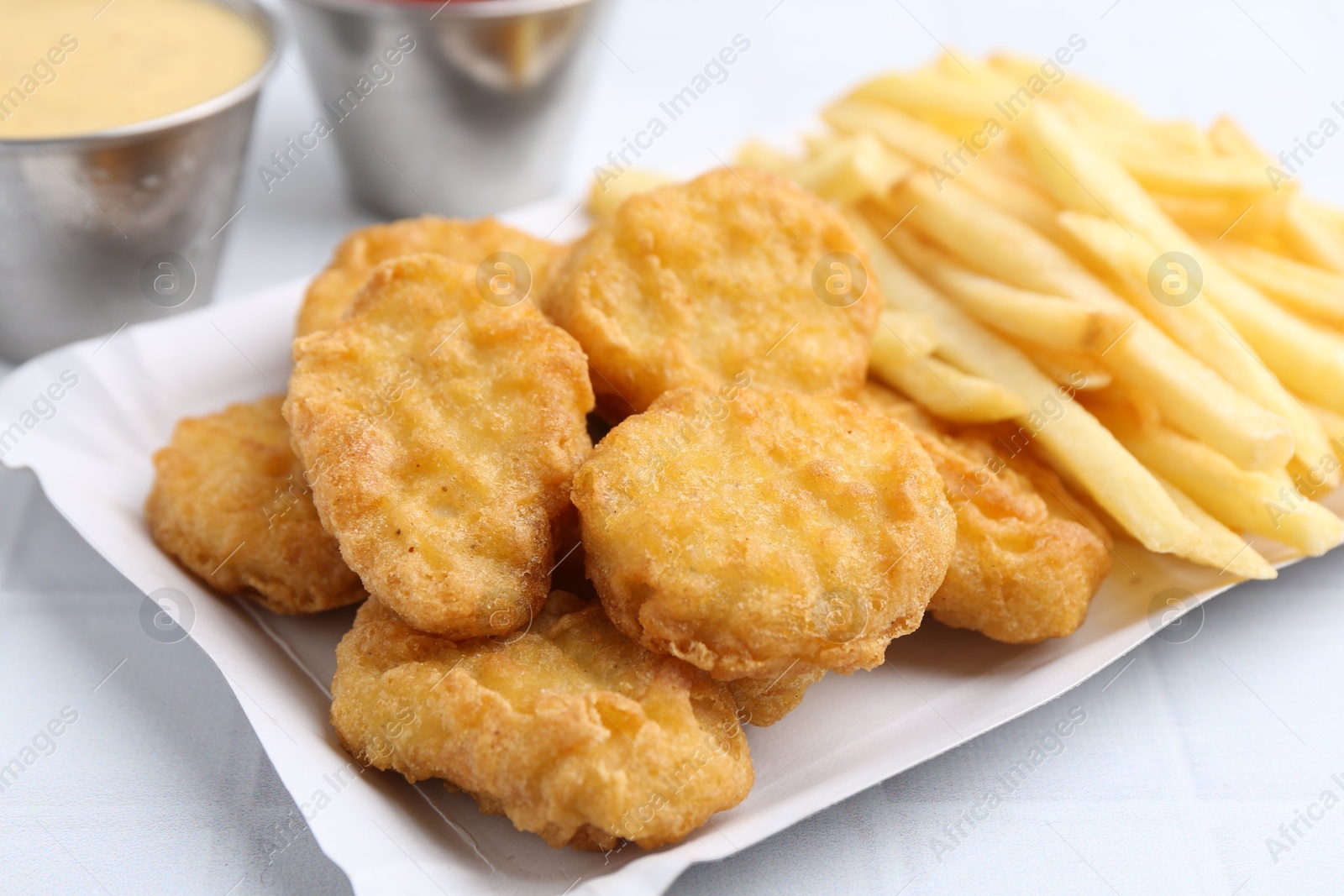Tasty chicken nuggets and french fries with sauce on white tiled table, closeup Photo of Tasty chicken nuggets and french fries with sauce on white tiled table, closeup