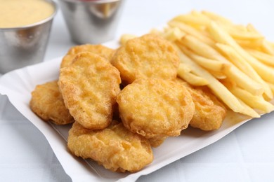Photo of Tasty chicken nuggets and french fries with sauce on white tiled table, closeup