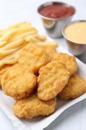 Photo of Tasty chicken nuggets and french fries with sauce on white table, closeup