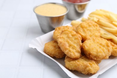 Tasty chicken nuggets and french fries with sauce on white tiled table, closeup. Space for text