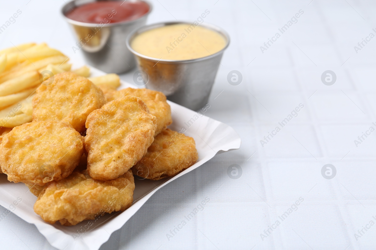 Tasty chicken nuggets and french fries with sauce on white tiled table, closeup. Space for text Photo of Tasty chicken nuggets and french fries with sauce on white tiled table, closeup. Space for text