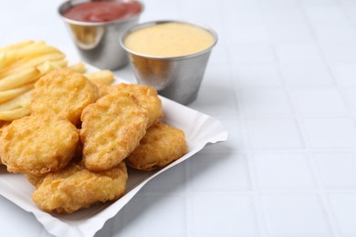 Photo of Tasty chicken nuggets and french fries with sauce on white tiled table, closeup. Space for text