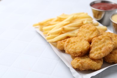 Photo of Tasty chicken nuggets and french fries with sauce on white tiled table, closeup. Space for text