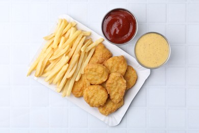 Photo of Tasty chicken nuggets and french fries with sauce on white tiled table, top view