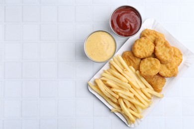 Photo of Tasty chicken nuggets and french fries with sauce on white tiled table, top view. Space for text