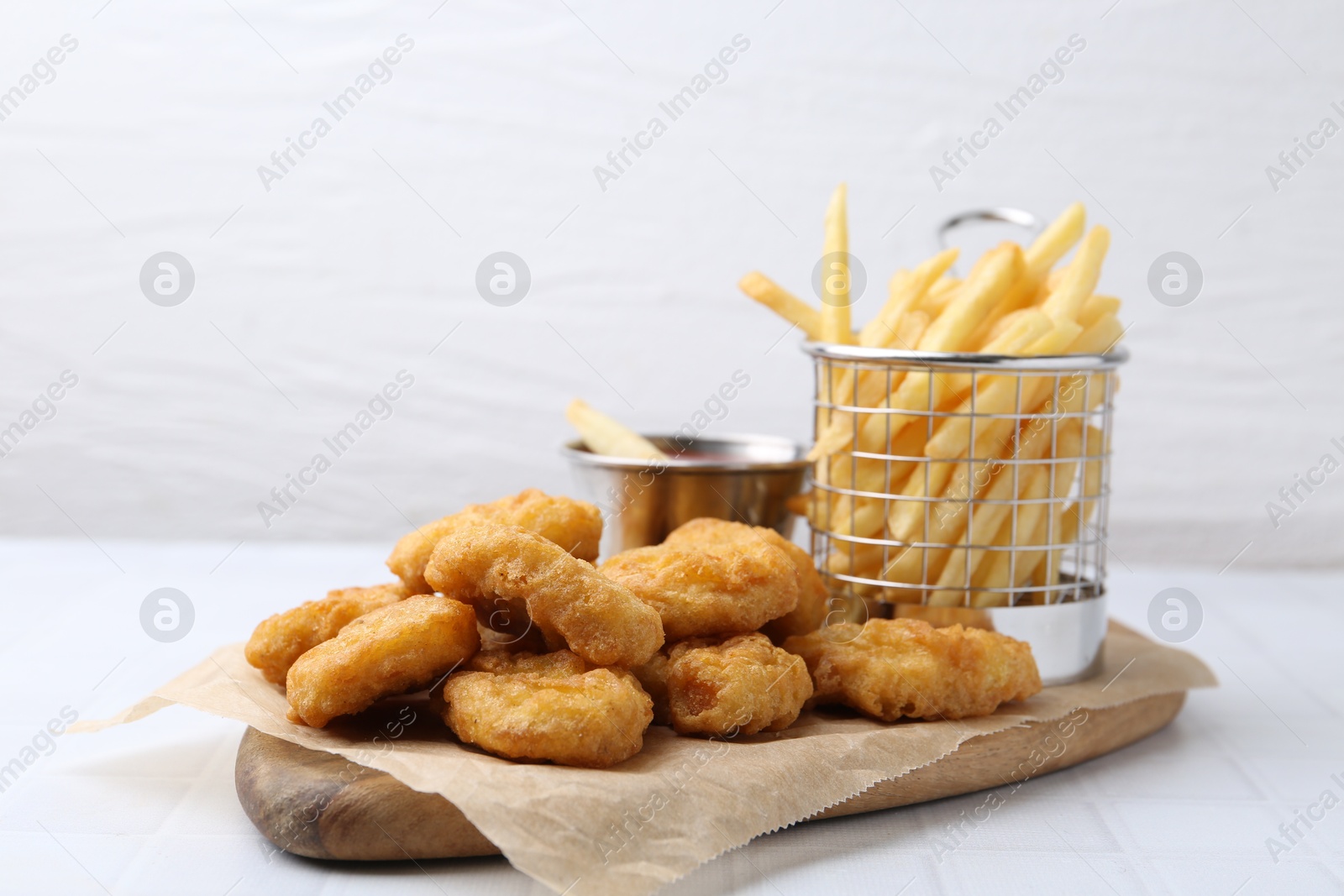 Tasty chicken nuggets, potato fries and sauce on white tiled table, closeup Photo of Tasty chicken nuggets, potato fries and sauce on white tiled table, closeup