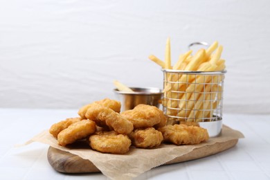 Photo of Tasty chicken nuggets, potato fries and sauce on white tiled table, closeup