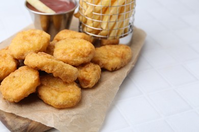 Photo of Tasty chicken nuggets, potato fries and ketchup on white tiled table, closeup. Space for text