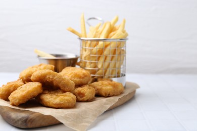 Photo of Tasty chicken nuggets, potato fries and sauce on white tiled table, closeup. Space for text