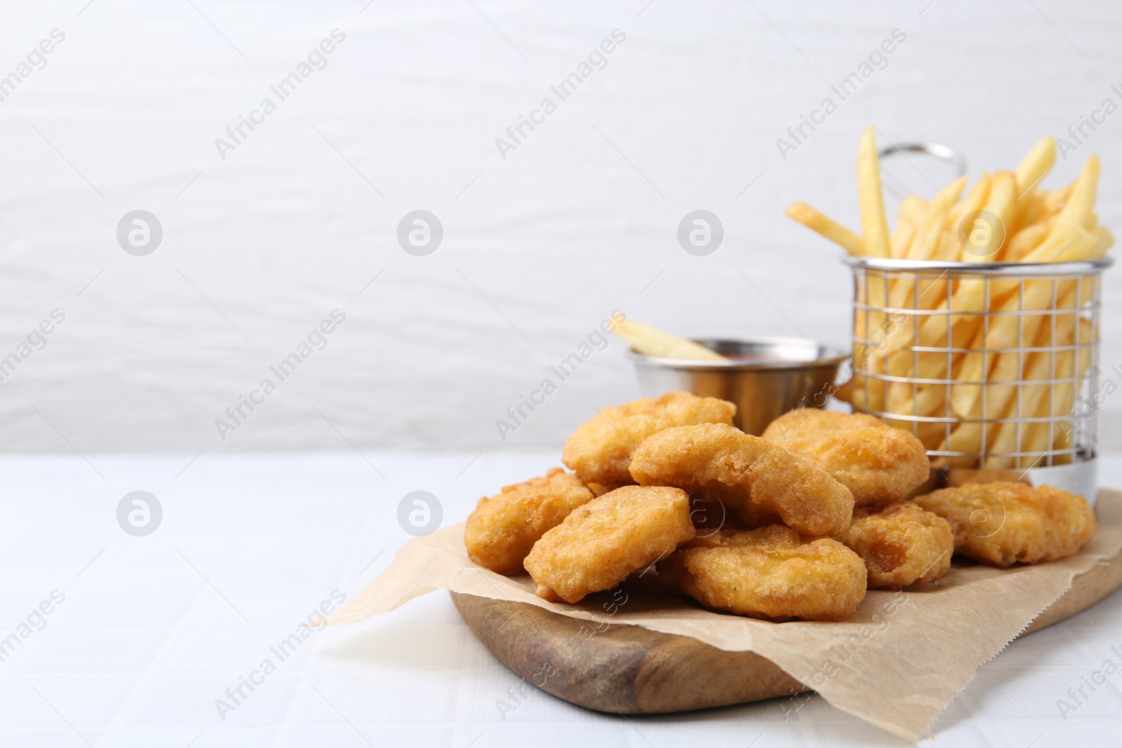 Tasty chicken nuggets, potato fries and sauce on white tiled table, closeup. Space for text Photo of Tasty chicken nuggets, potato fries and sauce on white tiled table, closeup. Space for text