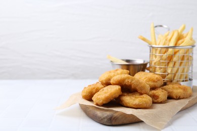 Photo of Tasty chicken nuggets, potato fries and sauce on white tiled table, closeup. Space for text