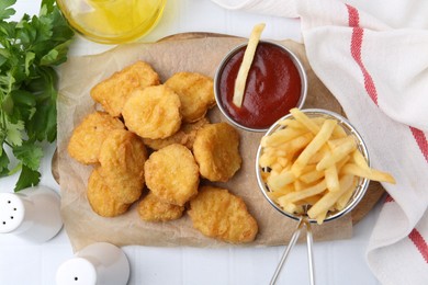 Photo of Tasty chicken nuggets, potato fries and ketchup on white tiled table, flat lay
