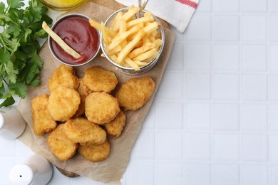 Photo of Tasty chicken nuggets, potato fries and ketchup on white tiled table, flat lay. Space for text