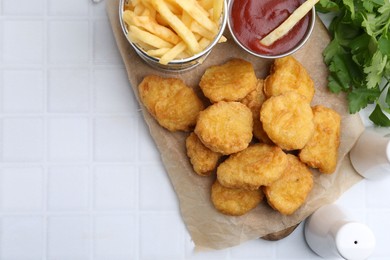 Photo of Tasty chicken nuggets, potato fries and ketchup on white tiled table, flat lay. Space for text