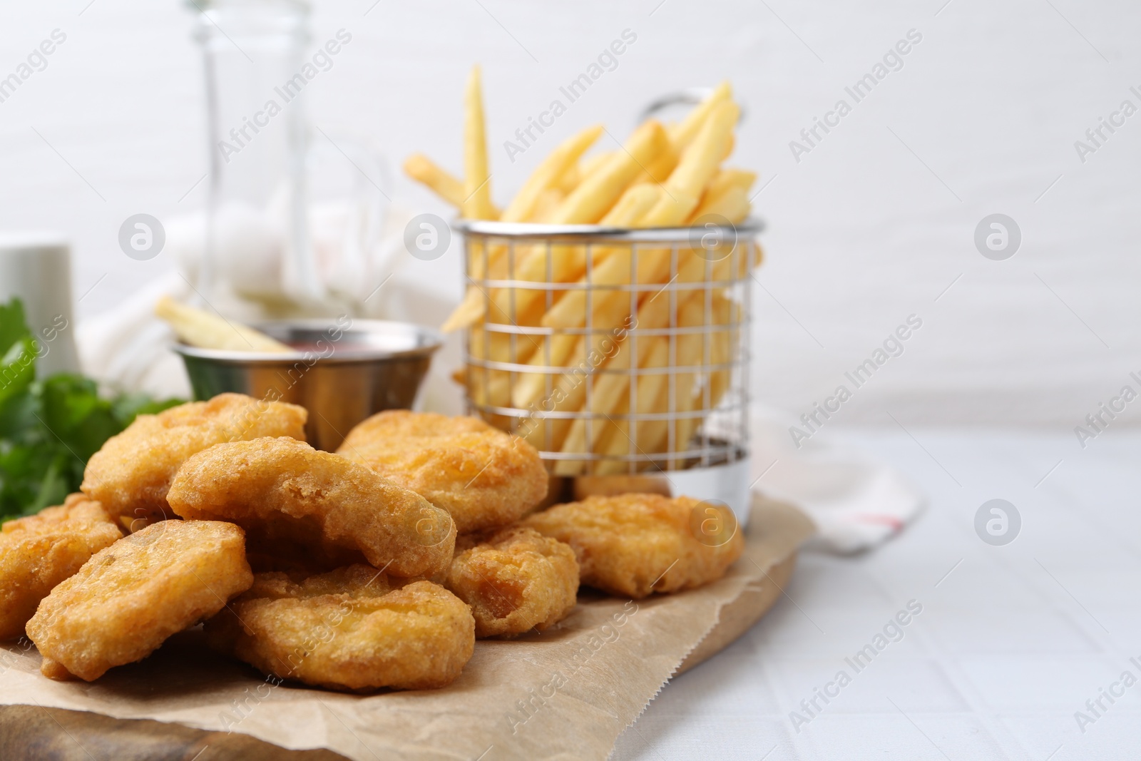 Tasty chicken nuggets, potato fries and sauce on white tiled table, closeup. Space for text Photo of Tasty chicken nuggets, potato fries and sauce on white tiled table, closeup. Space for text