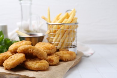 Photo of Tasty chicken nuggets, potato fries and sauce on white tiled table, closeup. Space for text