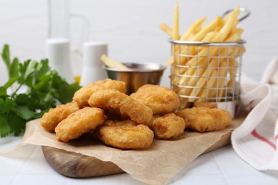 Photo of Tasty chicken nuggets, potato fries and sauce on white tiled table, closeup