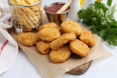 Photo of Tasty chicken nuggets, potato fries and ketchup on white tiled table, closeup