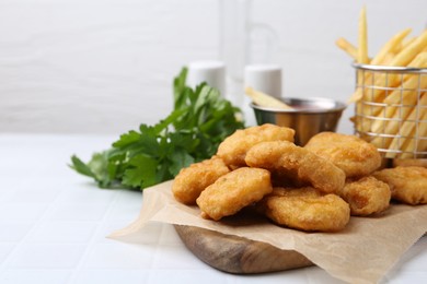 Photo of Tasty chicken nuggets, potato fries and sauce on white tiled table, closeup. Space for text