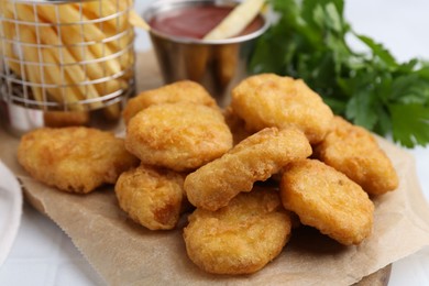 Photo of Tasty chicken nuggets, potato fries and ketchup on white tiled table, closeup