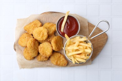 Photo of Tasty chicken nuggets, potato fries and ketchup on white tiled table, top view