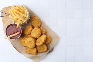Photo of Tasty chicken nuggets, potato fries and ketchup on white tiled table, top view. Space for text