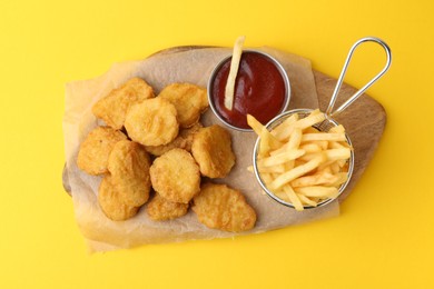Photo of Tasty chicken nuggets, potato fries and sauce on yellow background, top view