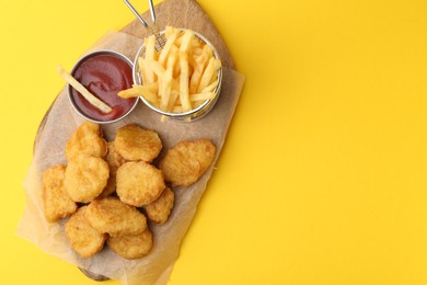Photo of Tasty chicken nuggets, potato fries and sauce on yellow background, top view. Space for text