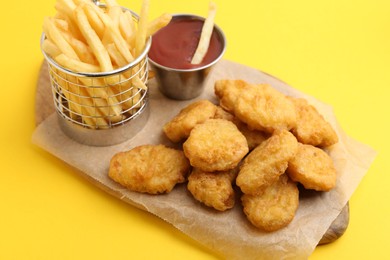 Photo of Tasty chicken nuggets, potato fries and sauce on yellow background, closeup