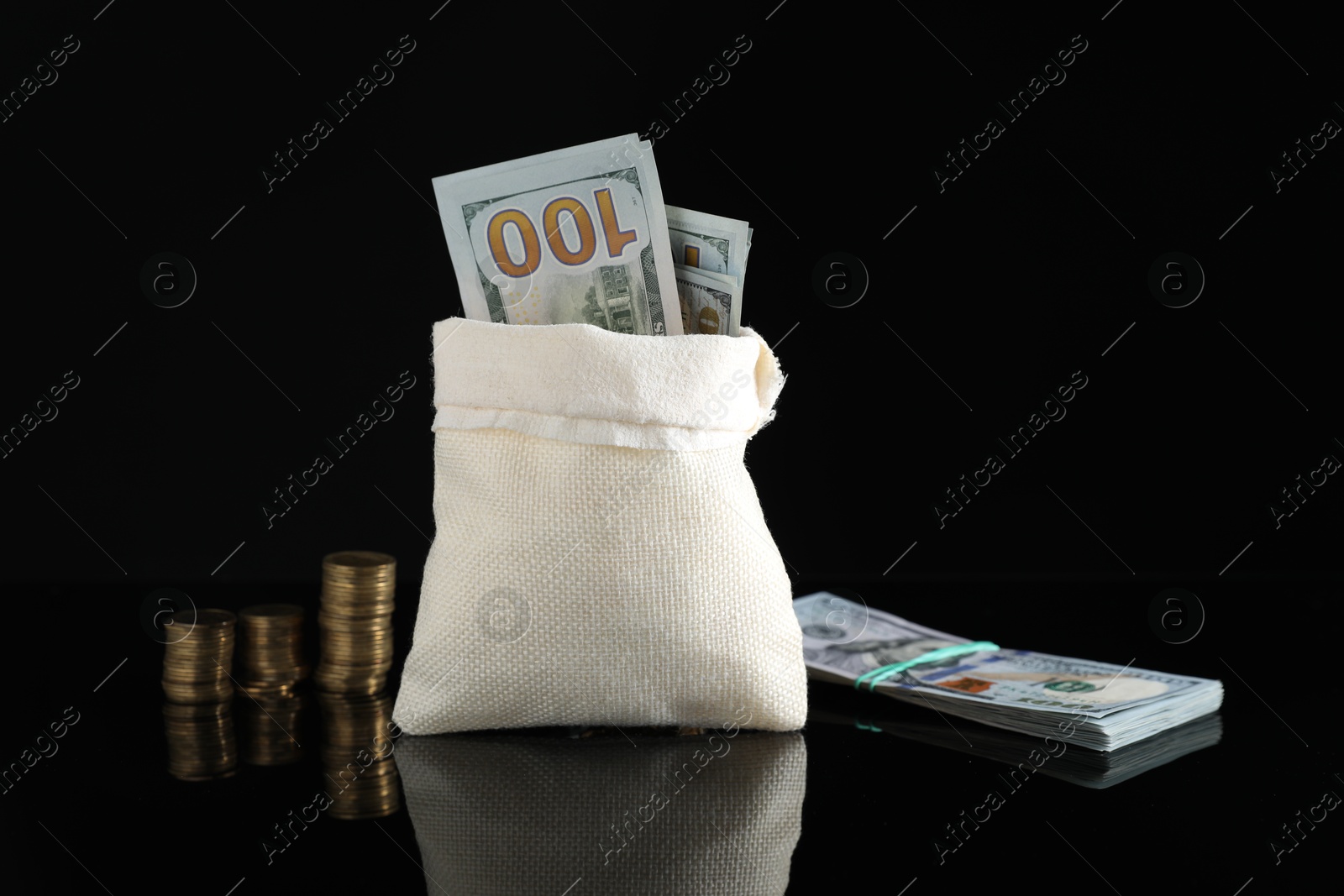 Photo of Burlap sack with dollar banknotes and stacked coins on dark mirror surface