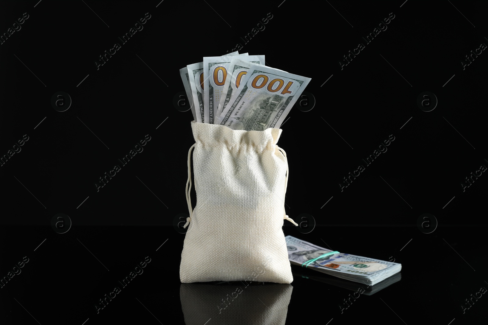 Photo of Burlap sack with dollar banknotes on dark mirror surface