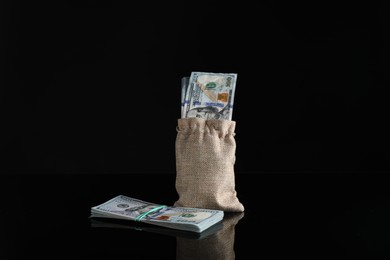 Photo of Burlap sack with dollar banknotes on dark mirror surface