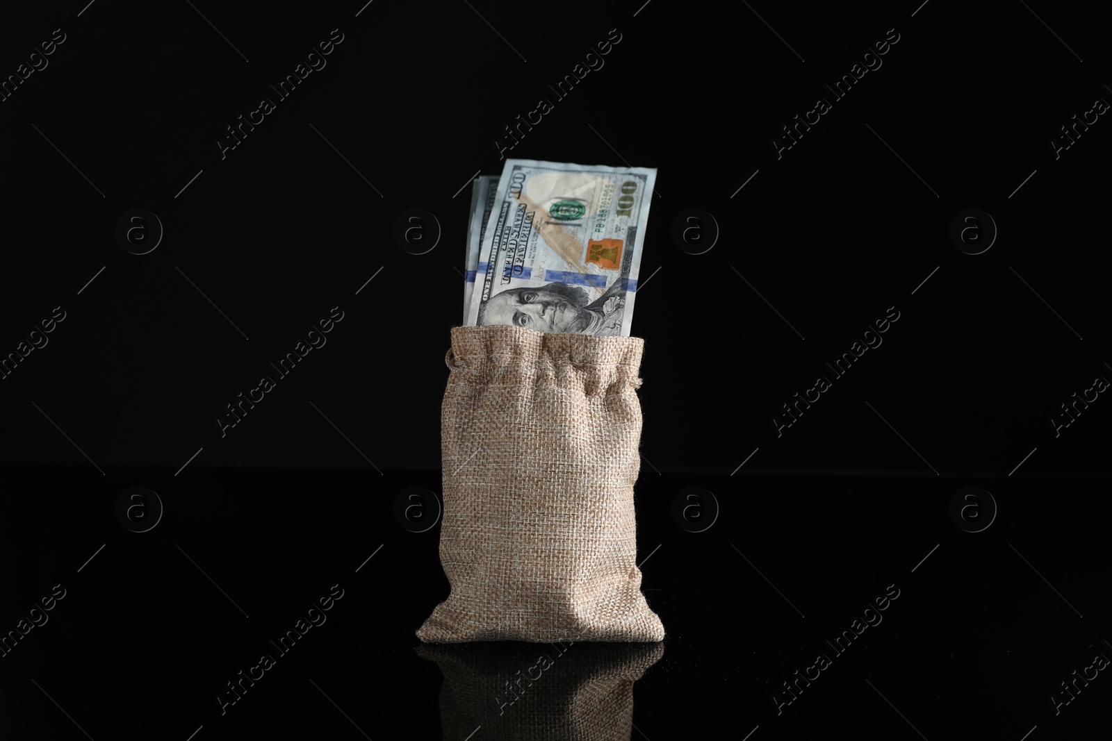 Photo of Dollar banknotes in burlap sack on dark mirror surface