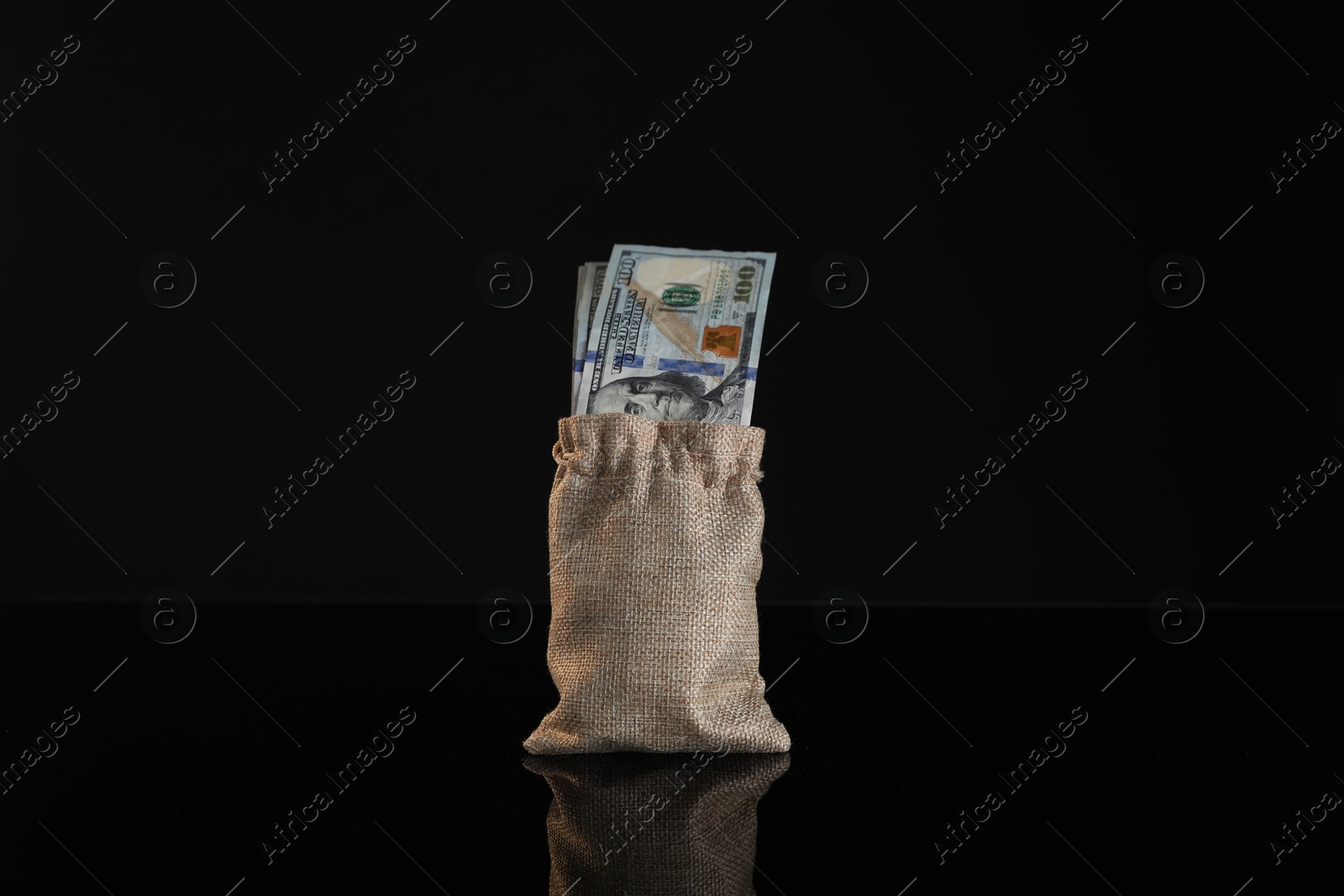 Photo of Dollar banknotes in burlap sack on dark mirror surface